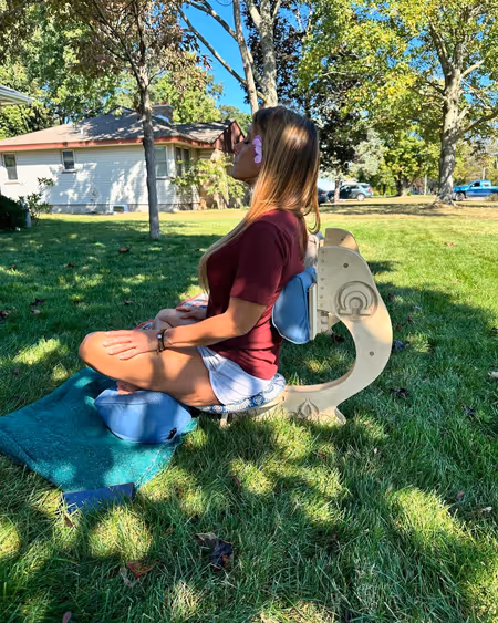 Jen, Realtor from Grand Rapids MI, using the OM Chair in a sunny park setting, seated in cross-legged meditation posture