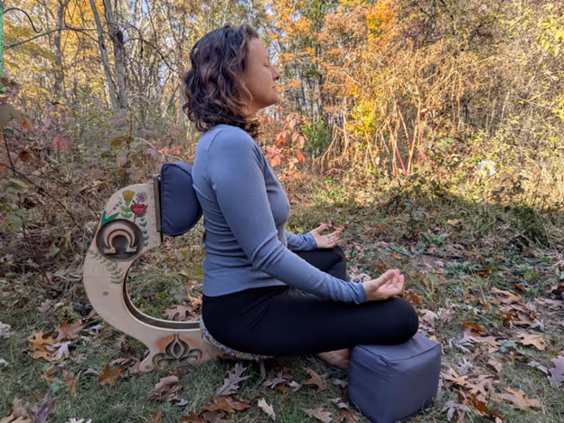Ashley meditating outdoors in autumn foliage, seated in a serene natural setting