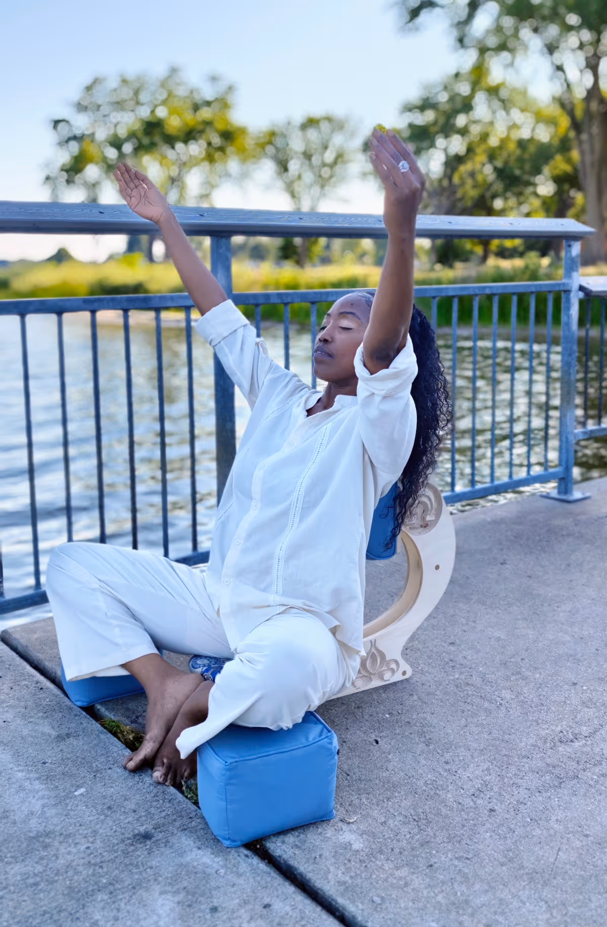 Woman seated upright in the OM Chair outdoors near a waterfront railing, demonstrating proper ergonomic meditation posture